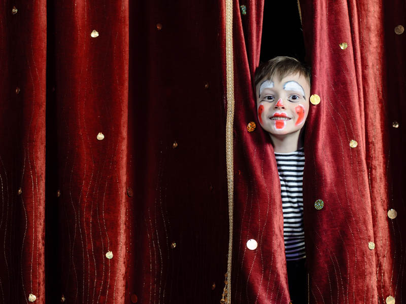 Enfant sortant de derrière un rideau rouge de théâtre en classe découverte