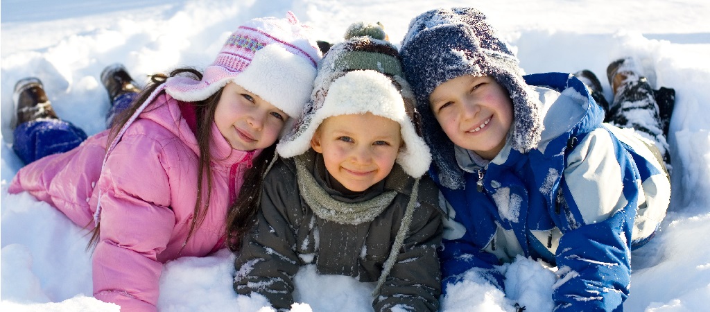 3 enfants en tenue d'hiver jouent et sourient dans la neige