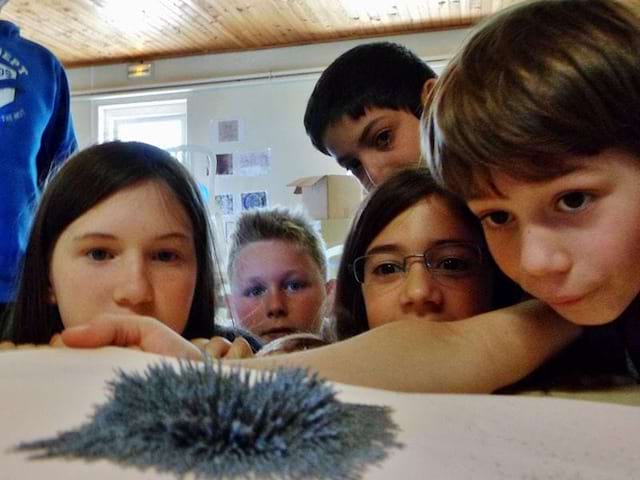 Enfants observant une expérience avec de la poudre magnétique en colonie de vacances d'été