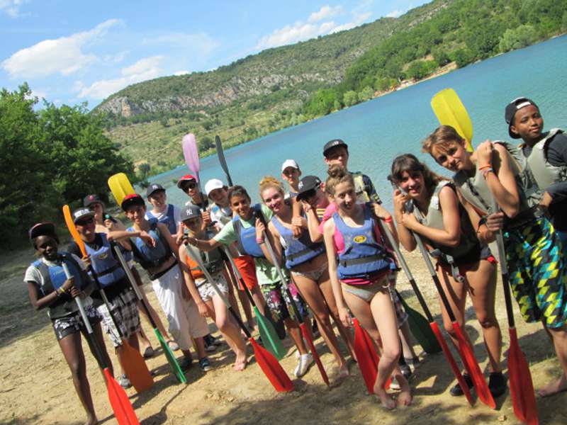 Groupe d'enfants devant le lac de Sainte Croix avec des pagaies et des gilets de sauvetages, prêts à aller faire du canoe kayak en colonie de vacances multiactivités cet été