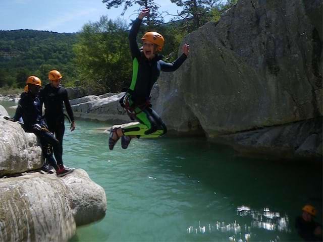 Enfants et ados sautant dans l'eau en combinaison de canyoning en colonie de vacances d'été dans le verdon