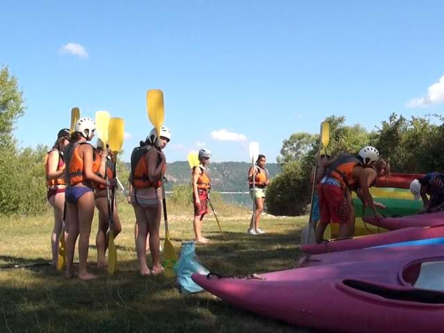 Enfants équipés de pagaie et gilet de sauvetage à côté de canoe kayak en colonie de vacances multiactivités dans le verdon cet été