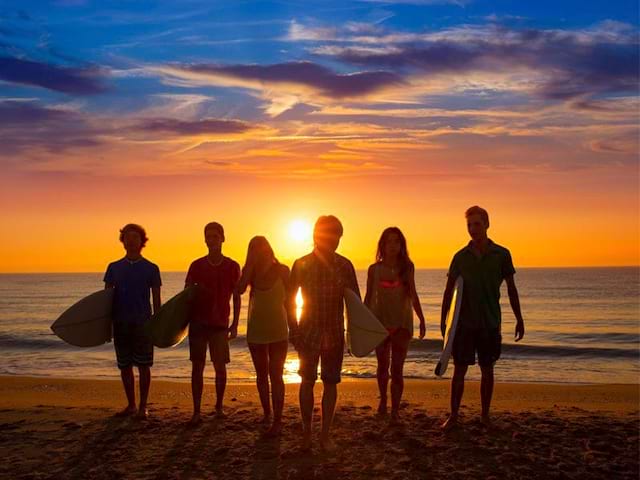 Groupe d'adolescents en bord de mer sous le coucher de soleil avec leur planche de surf en colonie de vacances d'été