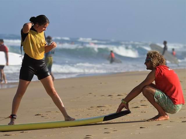 Moniteur de surf apprenant à une adolescente en colonie de vacances à faire du surf