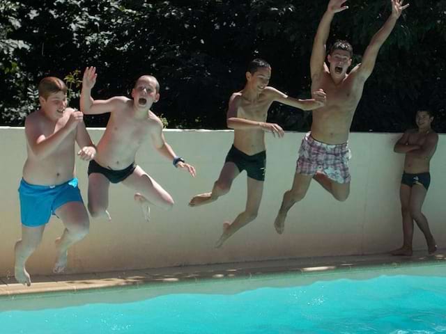 Groupe d'enfants sautant dans la piscine en colonie de vacances à la montagne