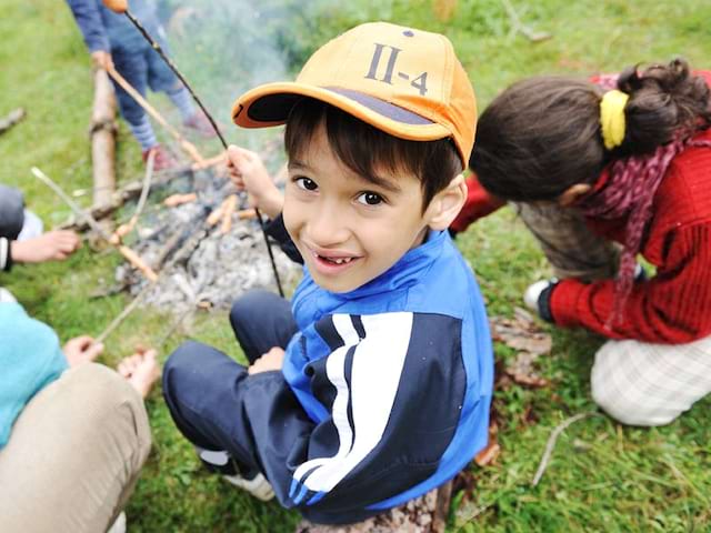 Enfant de 6 ans faisant griller un chamallow sur le feu en colonie de vacances été