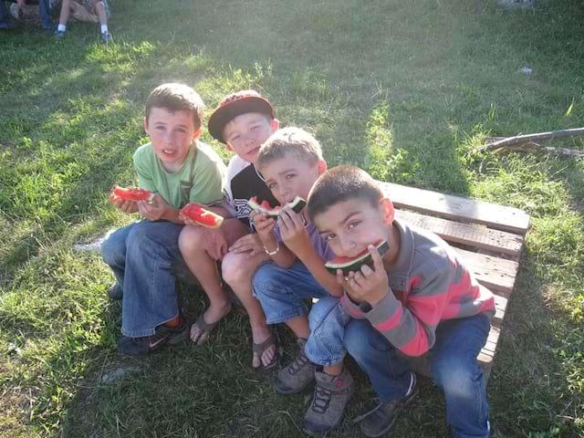 Groupe d'enfants sur un banc mangeant de la pastèque en colonie de vacances 