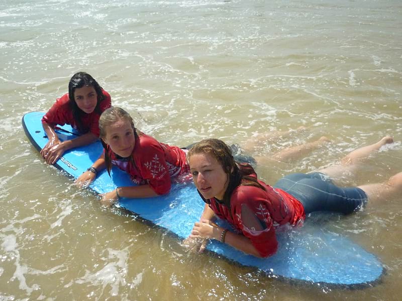 Trois jeunes filles à l'océan accoudées sur une planche de surf en colonie de vacances