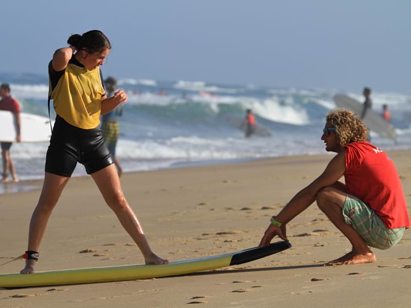 Adolescente apprenant la bonne posture pour faire du surf avec un moniteur de surf 