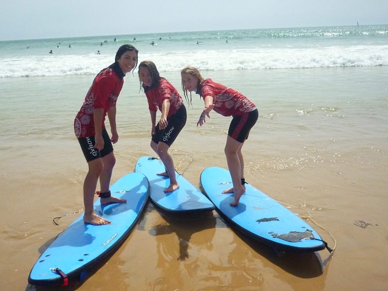 Trois jeunes apprenant à tenir debout sur un surf en colonie de vacances cet été