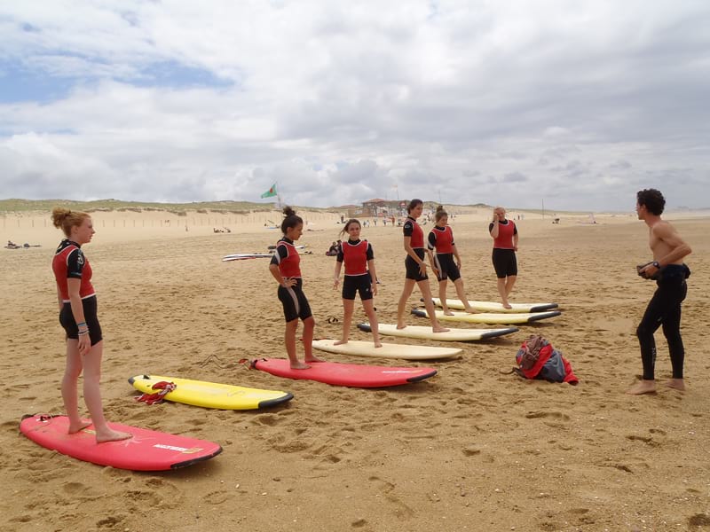 Groupe d'enfants sur la plage apprenant à tenir debout sur une planche de surf