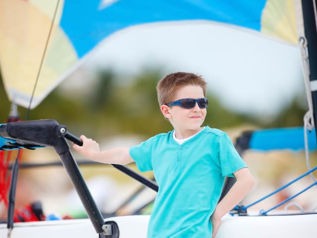 jeune garçon portant des lunettes de soleil à la plage en colonie de vacances surf