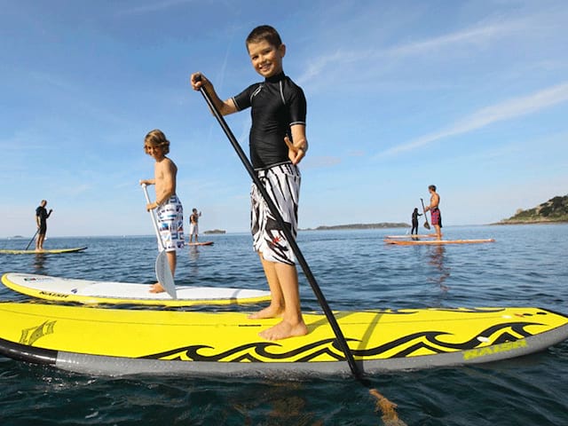 Enfants apprenant à faire du stand up paddle en colonie de vacances cet été