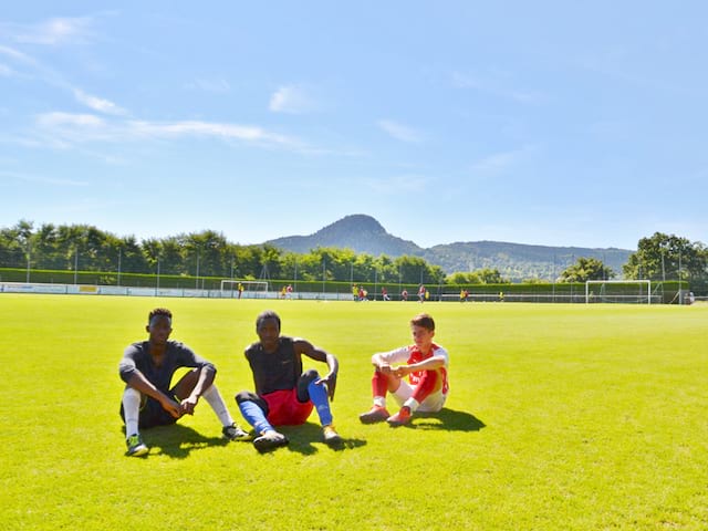 ados assis sur un terrain de football en stage sportif cet été