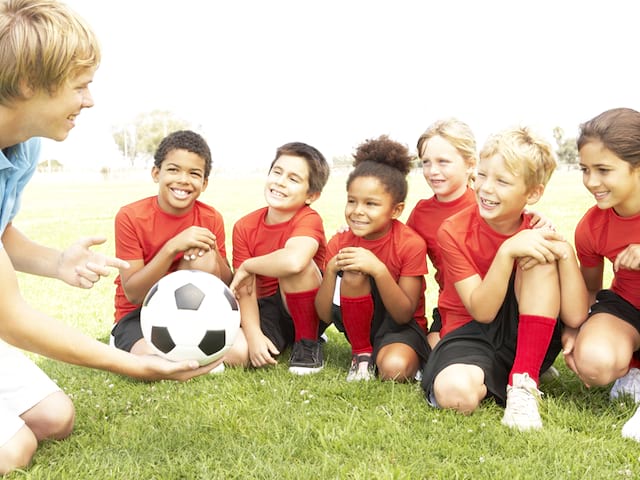 Enfants apprenant à jouer au football avec un entraineur cet été en stage sportif