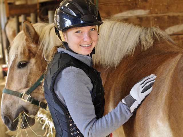 Jeune fille brossant son cheval en colonie de vacances d'été à la montagne