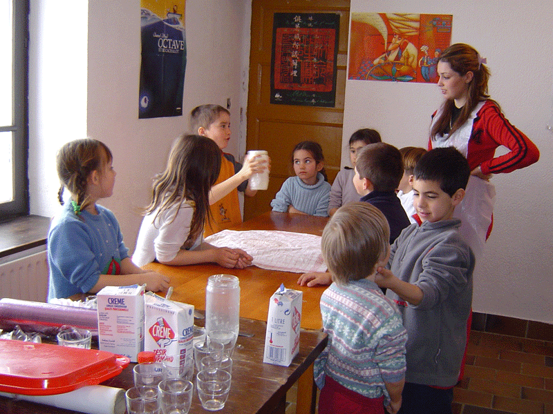 Groupe de très jeunes enfants et leur animatrice de colonie apprenant à cuisiner en colo