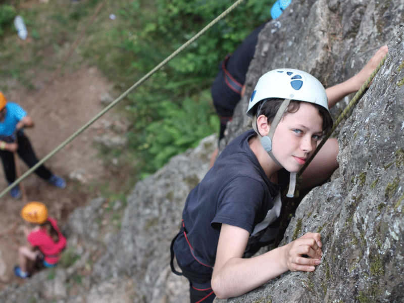 jeune garçon faisant de l'escalade en colonie de vacances d'été à la montagne 