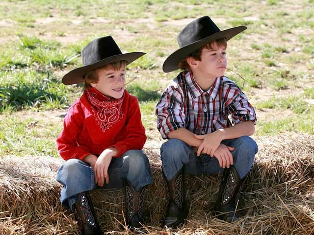 Deux garçons déguisés en cow-boys assis sur une botte de paille pour la colo d'été