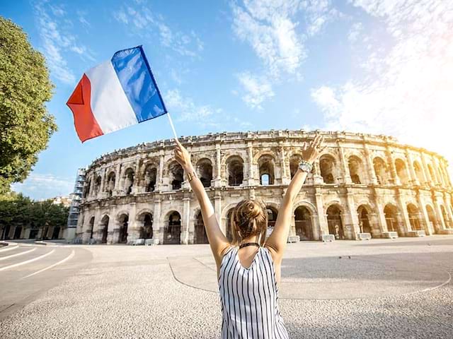 Un adolescent devant les Arènes de Nîmes, tenant dans la main un drapeau français en été