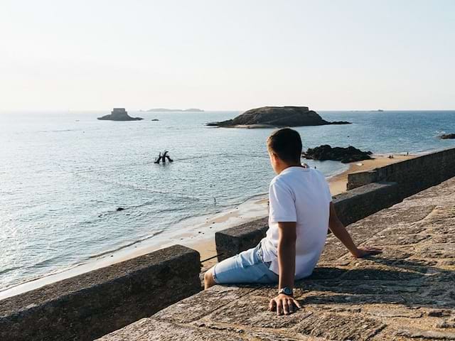 Jeune garçon qui regarde le coucher de soleil lors de sa colo en itinérance en Bretagne durant l'été