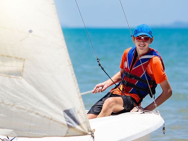 Un ado en colonie de vacances faisant de la planche à voile en été