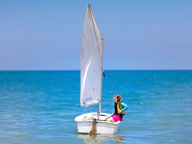 Fillette apprenant à faire de l'optimist en colonie de vacances cet été