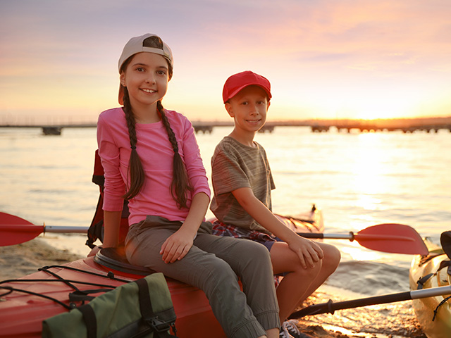 deux pré ados au coucher du soleil assis sur un canoë kayak au bord de l'eau