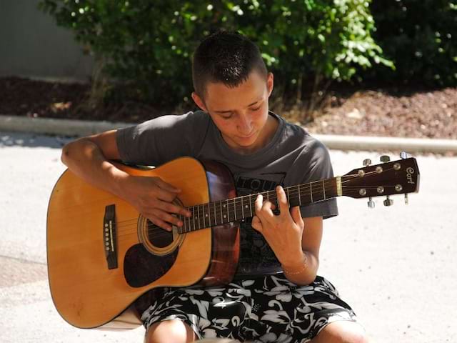 Jeune garçon qui joue de la guitare cet été en colo artistique