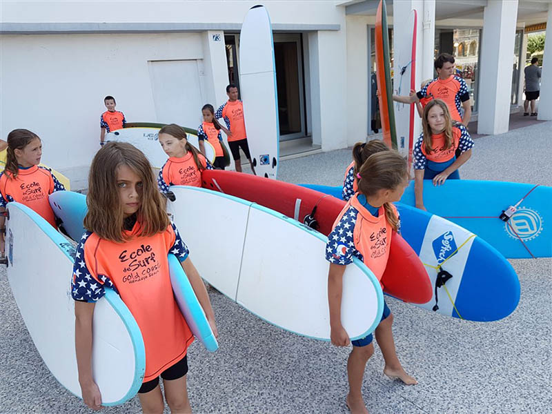 Groupe de jeunes enfants qui portent leur surf en colo de vacances à Anglet