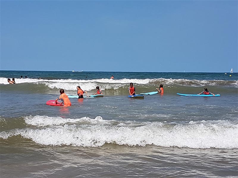 Jeunes enfants en colo de vacances qui font du surf en petit groupe à l'océan
