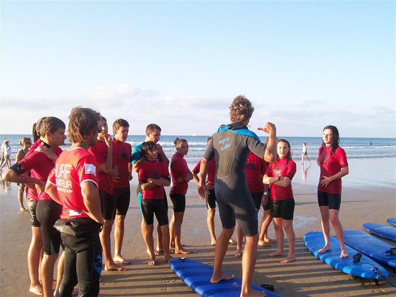 Groupe de jeunes avec leur prof de surf qui apprennent la théorie et la pratique de l'activité