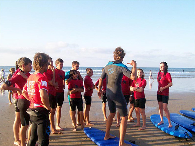 groupe d'ados avec planche de surf sur la plage en colo cet été