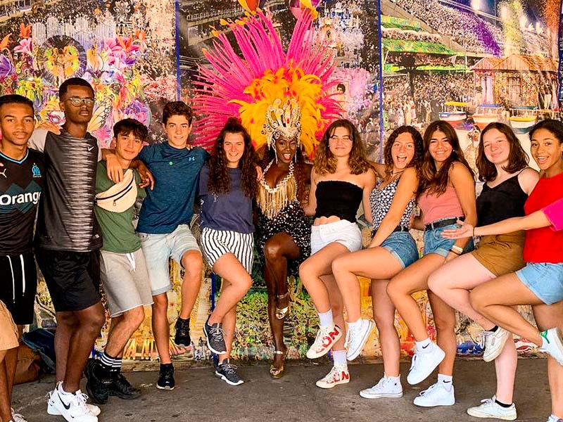 Groupe d'ados qui prend la pose lors de leur colo de vacances au Brésil cet été, en compagnie d'une danseuse traditionnelle 