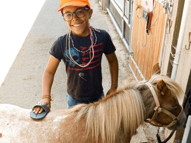 Jeune garçon qui s'occupe de sa monture en colo de vacances spéciale Poney cet été