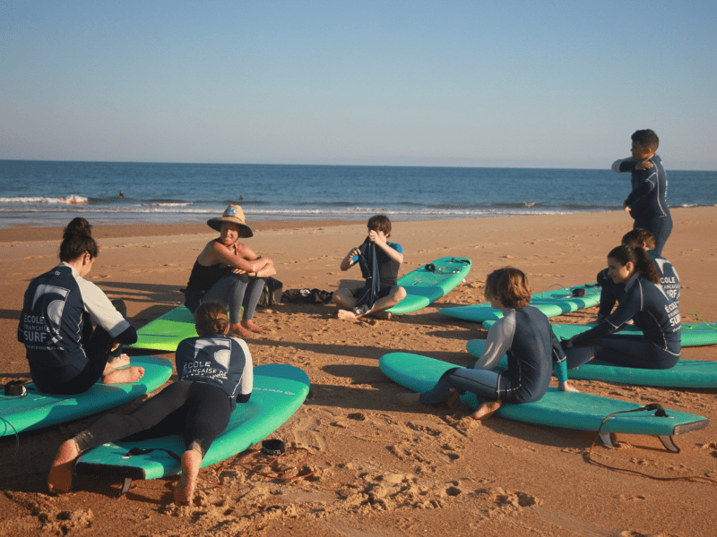 Groupe de jeunes sur la plage qui écoutent leur leçon de surf 