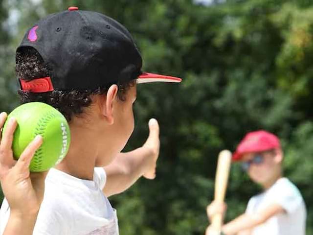 enfant lancant une balle de baseball en colonie de vacances cet été