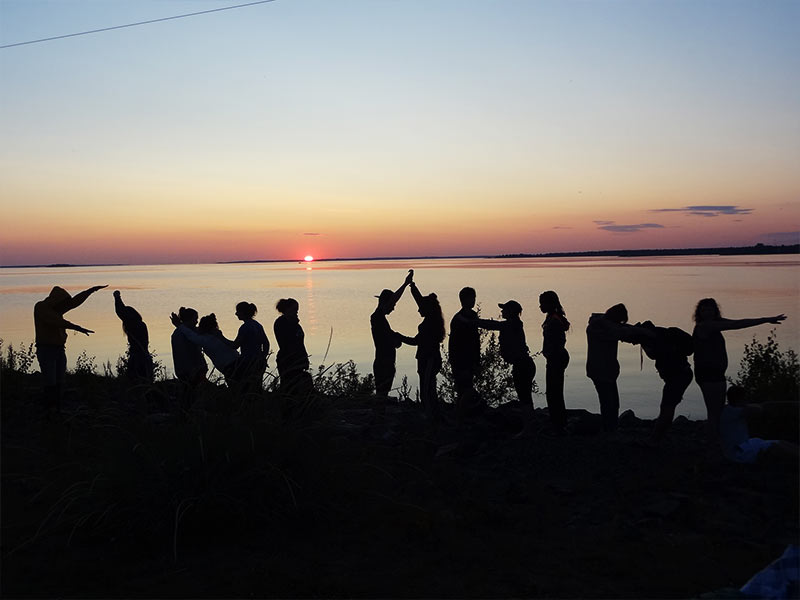 Groupe d'ados au bord de la mer qui profitent d'un coucher de soleil lors de leur colo en Finlande et en Estonie