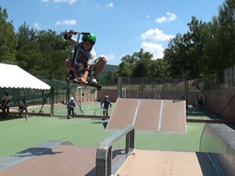 Enfants faisant de la trottinette sur un skatepark en colonie de vacances d'été 