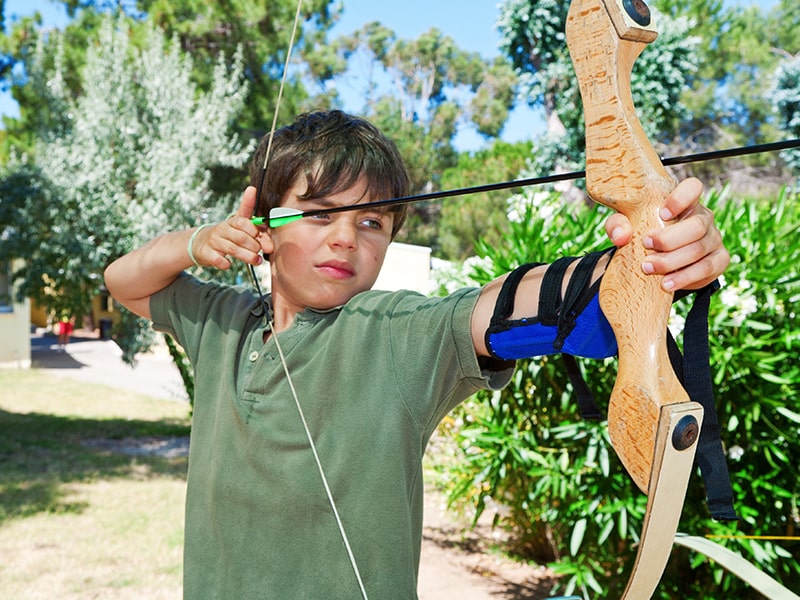 Jeune garçon qui pratique le tir à l'arc en colo de vacances Montagne & Nature
