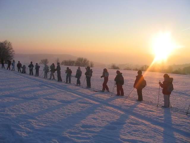 Enfants faisant du ski de fond sous un coucher de soleil en colonie de vacances