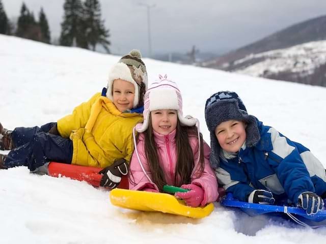 portrait de trois enfants avec leur luge en colonie de vacances à la neige