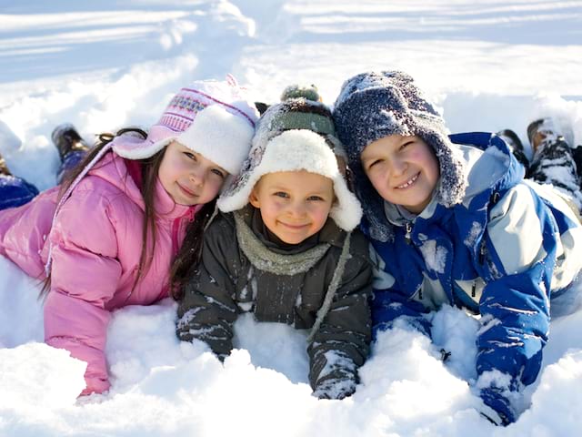 Trois jeunes enfants couchés dans la neige et souriants