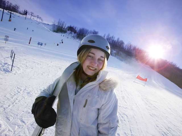 Jeune fille qui sourit avec son surf en colonie de vacances à la neige