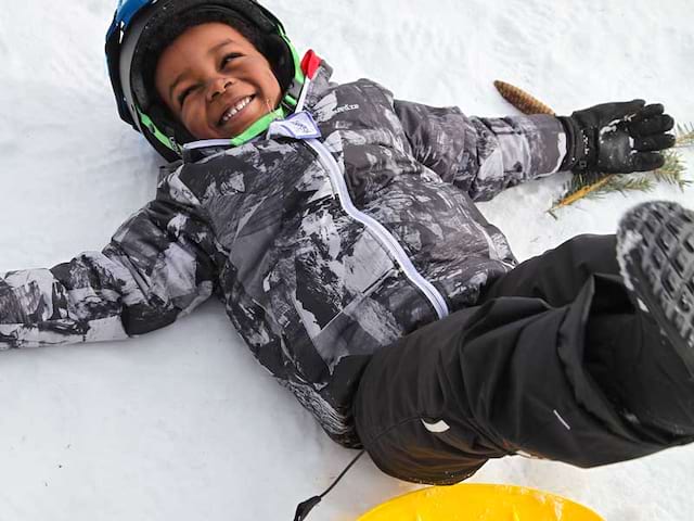 Enfant qui s'amuse dans la neige en luge en colonie de vacances