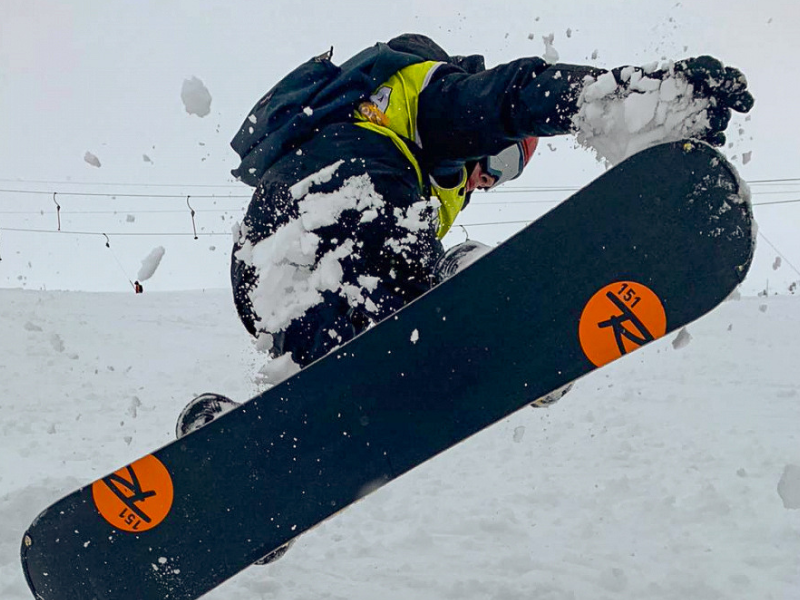 Jeune garçon qui réalise une figure en snowboard durant sa colo de vacances cet hiver 