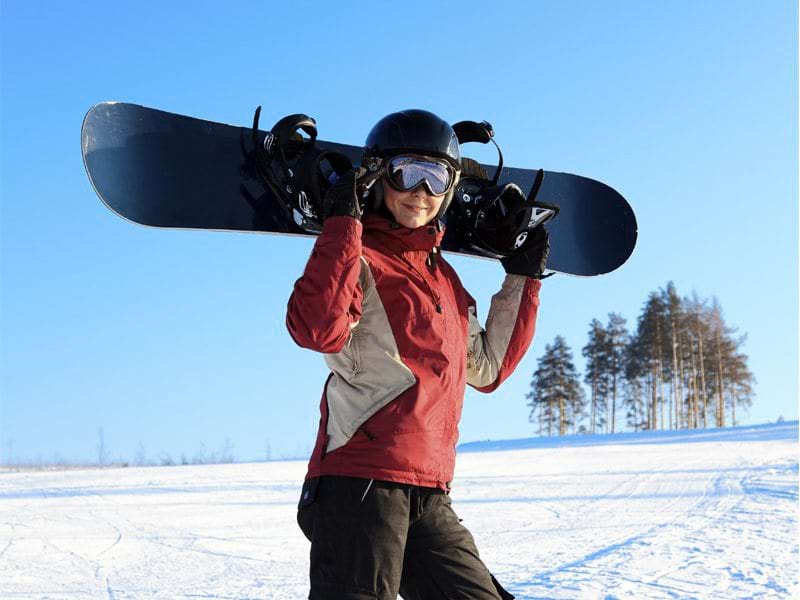 ado portant sa planche de surf en colo à neige