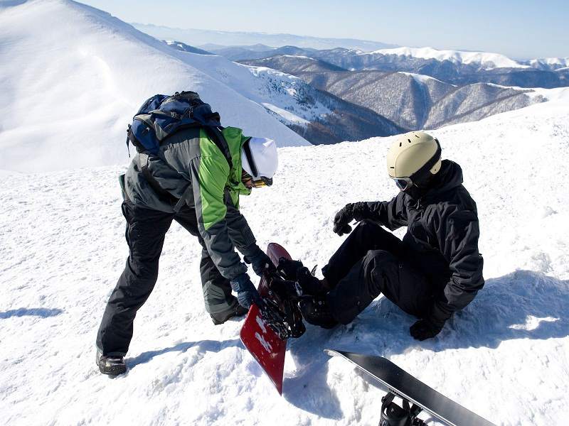 ado aidant son ami à chausser son snowboard en colo à courchevel cet hiver