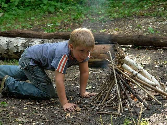 Petit garçon en train d'observer un feu de camp