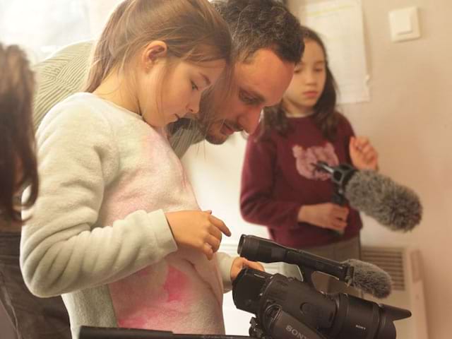 Animateur apprenant à une fillette de colo à se servir d'une caméra professionnelle